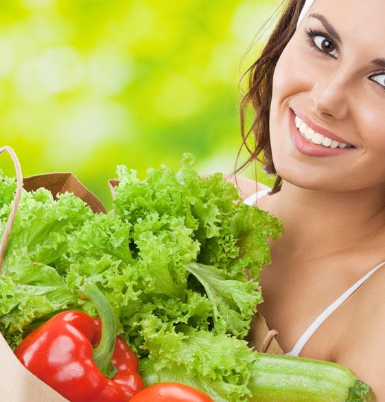 Portret szczęśliwej uśmiechniętej młodej pięknej kobiety w stroju fitness trzymającej torbę na zakupy spożywcze ze zdrową wegetariańską żywnością, na świeżym powietrzu